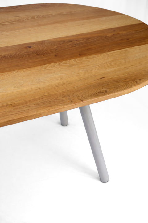 Detalle de la mesa Pilote de ANKA Taller con cubierta ovalada de madera natural y pata metálica inclinada, fotografía sobre fondo blanco.